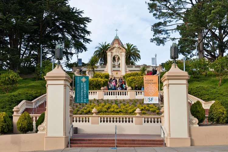 A stairway leading to a chapel with a statue, surrounded by trees and bushes, at the University of San Francisco campus.
