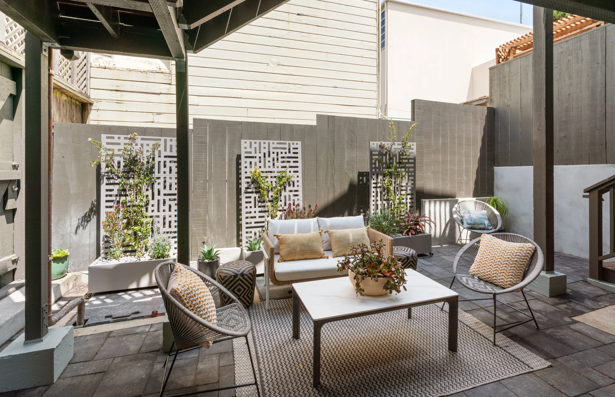 Outdoor patio area with sitting furniture, potted plants, and a decorative privacy fence.
