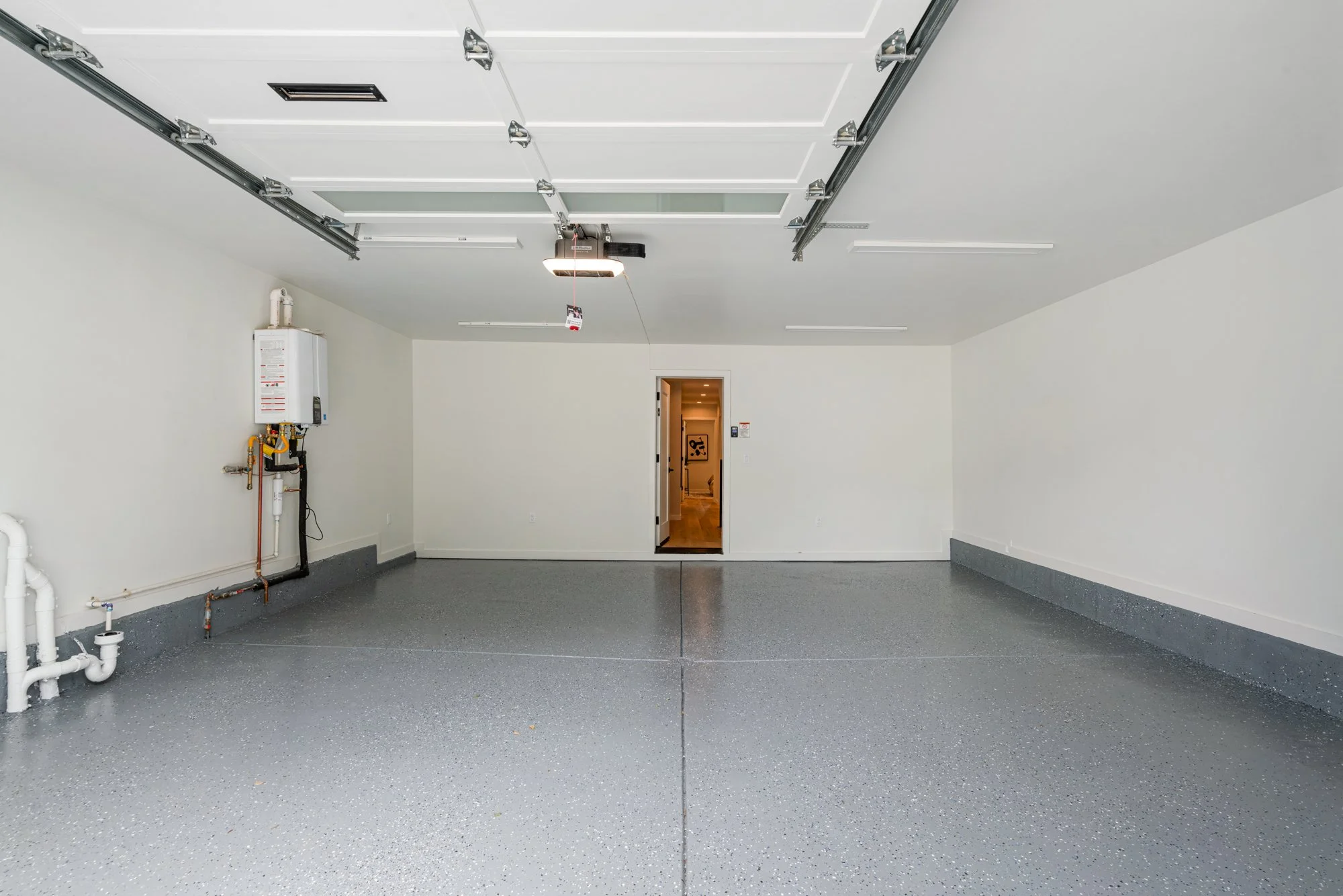 Empty two-car garage with a side door leading inside, white walls, gray speckled epoxy floor, and an electric garage door opener.