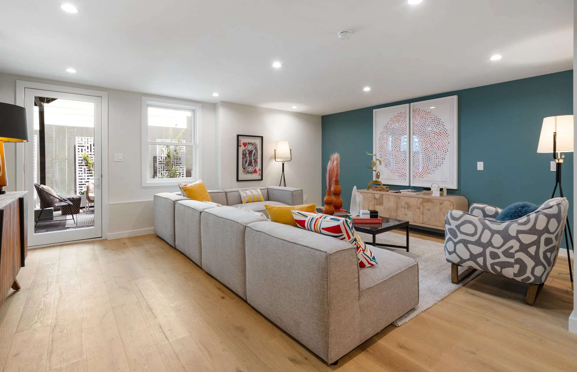 Modern living room with a large white sectional sofa, patterned armchair, artwork, and decorative accents, with a door leading to an outdoor patio.