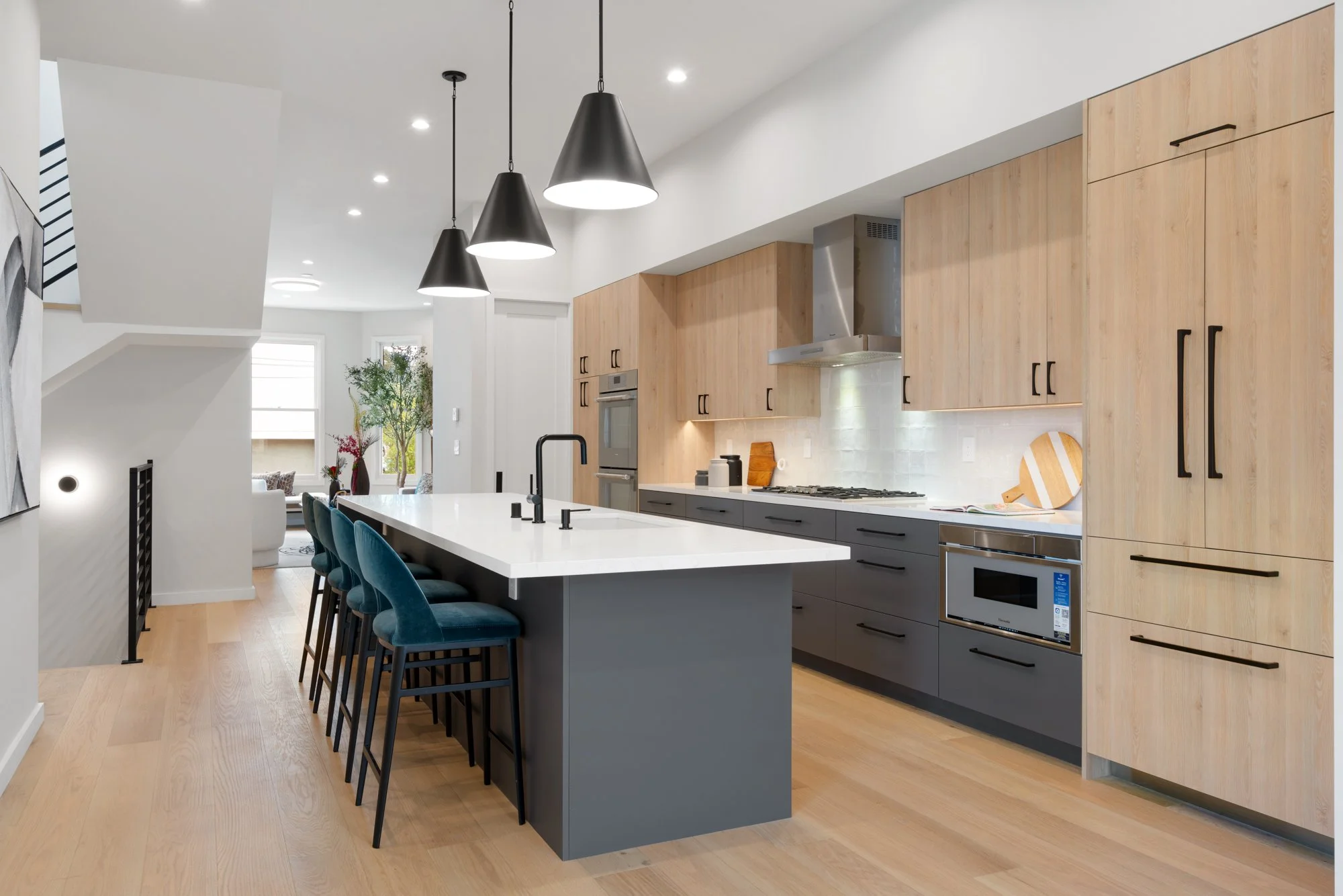 Modern kitchen with wooden cabinets, gray lower cabinets, a white marble island with black bar stools, black pendant lights, and built-in appliances.
