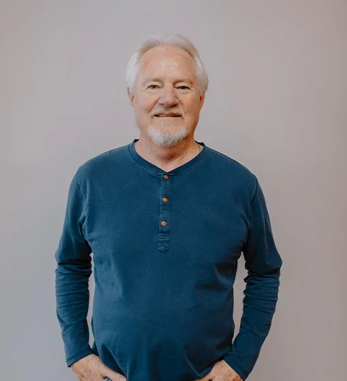 An older man with a gray beard and short white hair wearing a blue long-sleeve shirt.