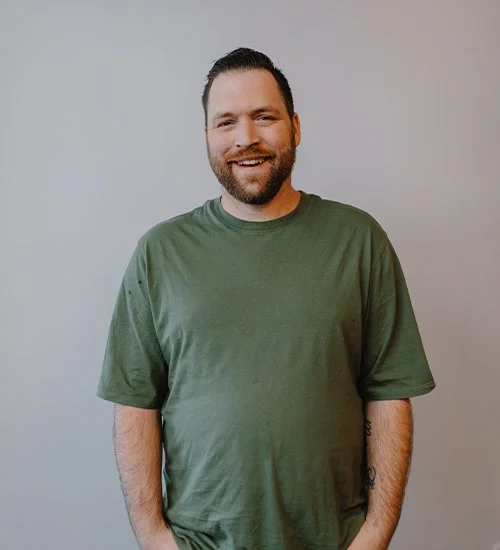 Man wearing a green t-shirt smiling in front of a plain background.