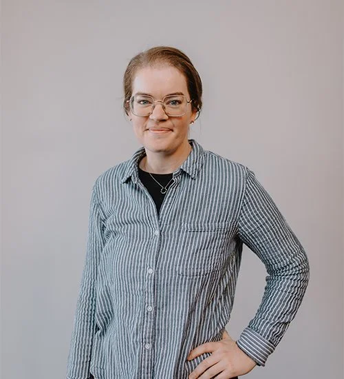 Person with glasses and striped shirt posing against a plain background.