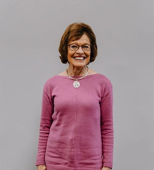 Smiling woman wearing glasses and a pink sweater against a plain background.