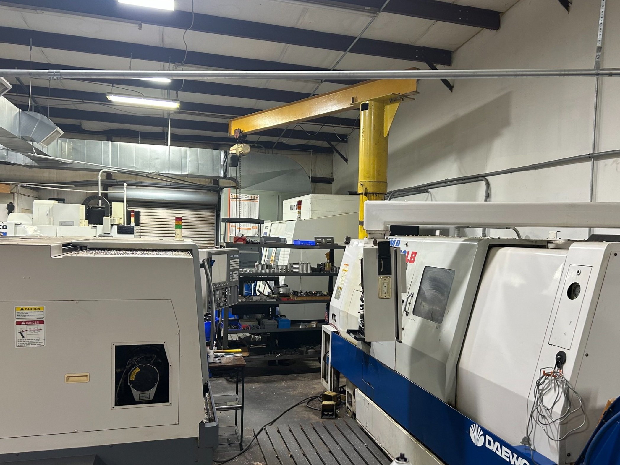 Industrial manufacturing workshop with large machinery, control panels, and workbenches under a high ceiling with exposed beams and ductwork.