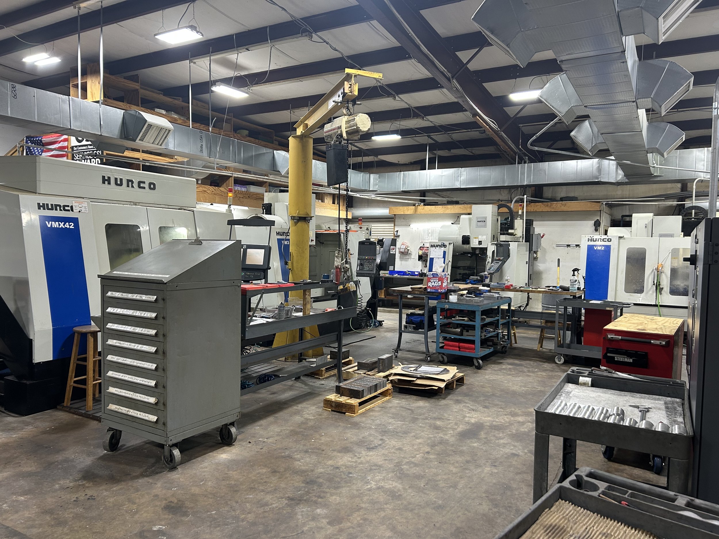 Industrial machine shop with several CNC machines, workbenches, tools, and equipment in a spacious workshop with overhead lighting.