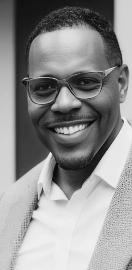 Black and white photo of a smiling man wearing glasses, a suit jacket, and a collared shirt.