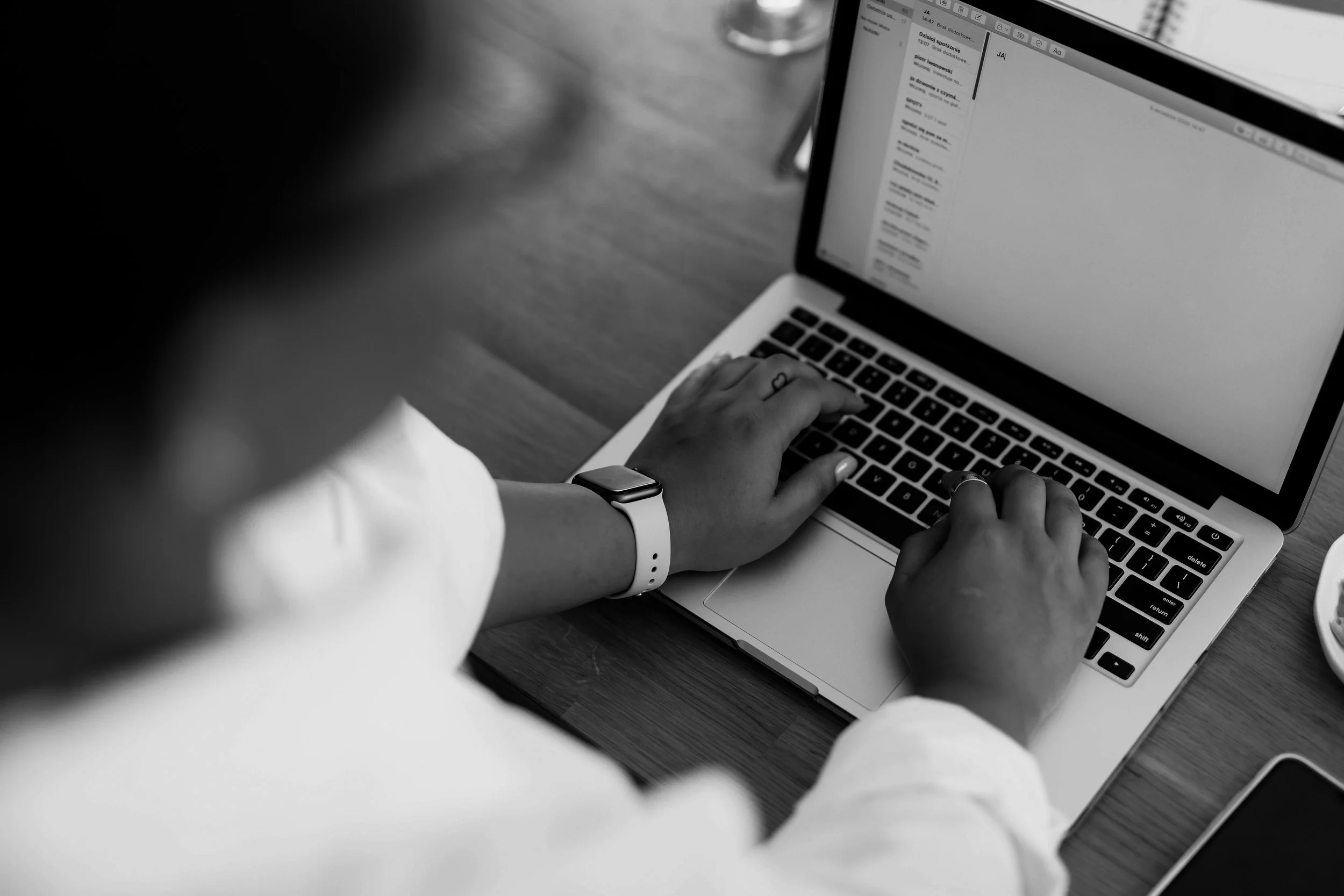 hands with an apple watch on typing on laptop on a desk in black and white