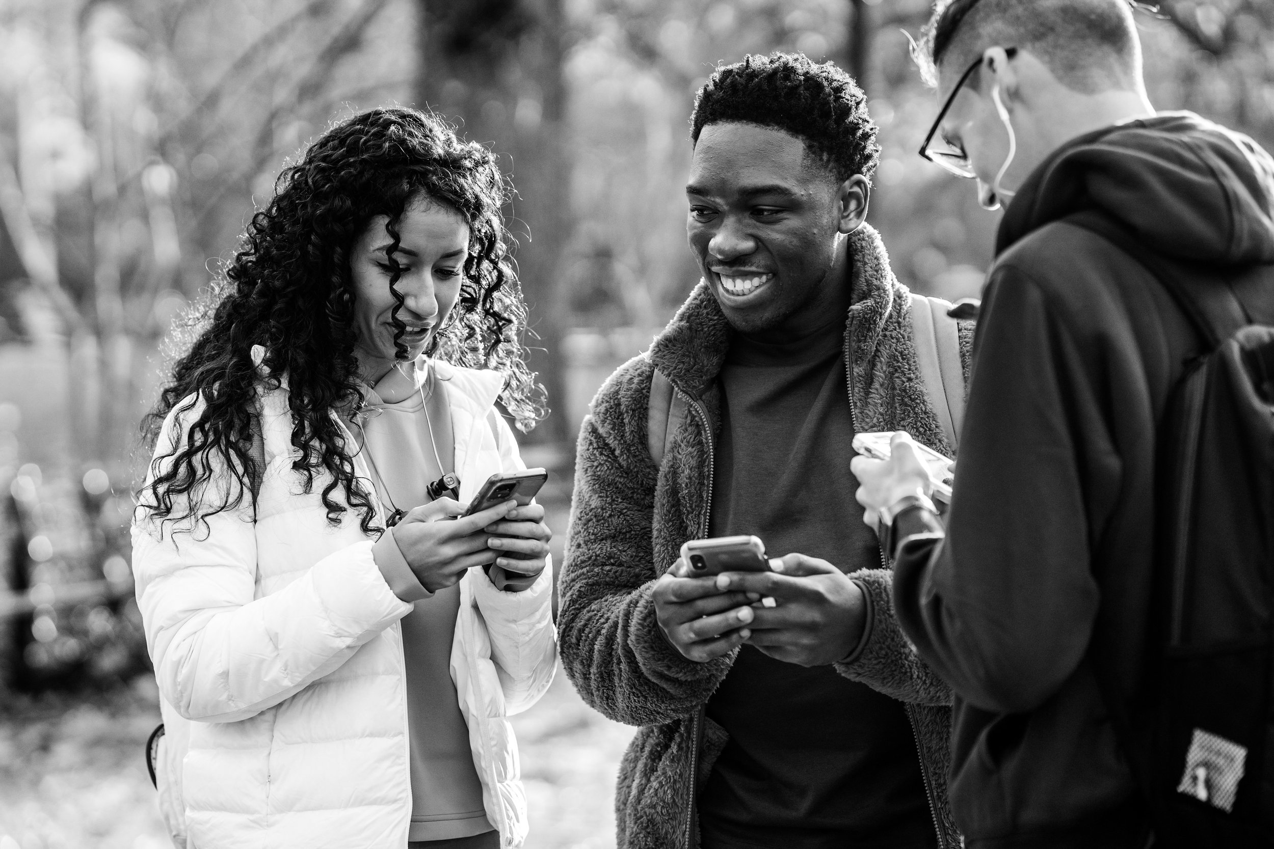black and white photo of a group of 3 teens hanging out with phones in their hands while smiling