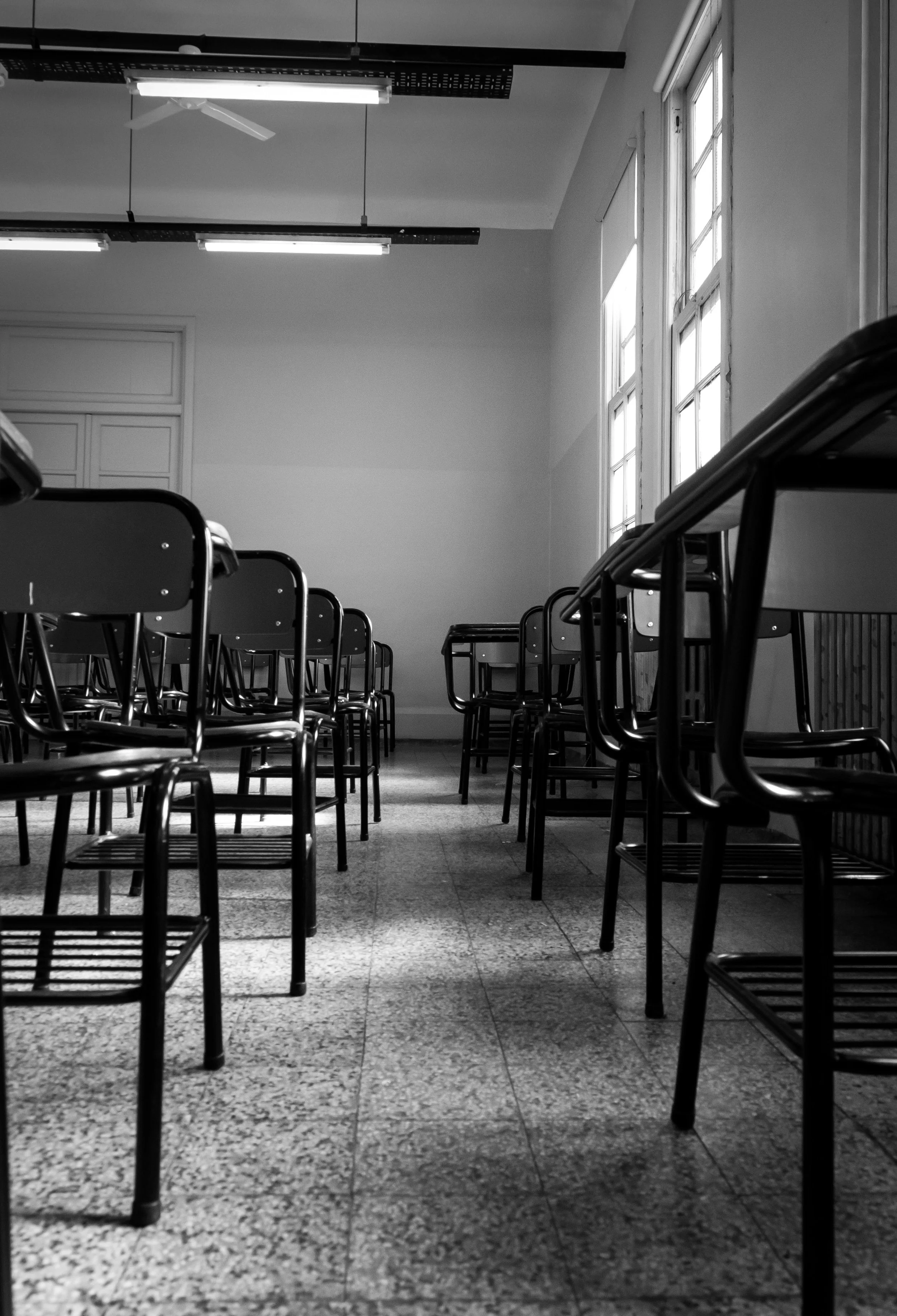 black and white photo of empty school desks lined up in a classroom
