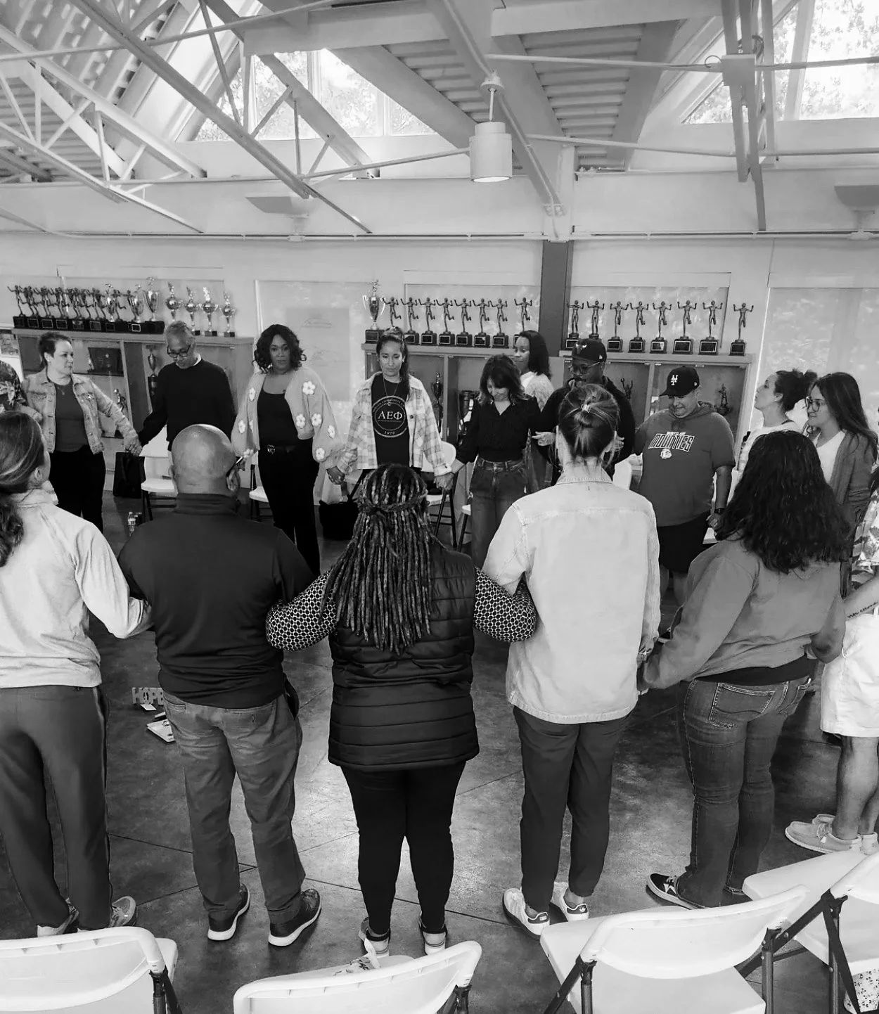 black and white photo of adult educators holding hands in a circle during a professional development session