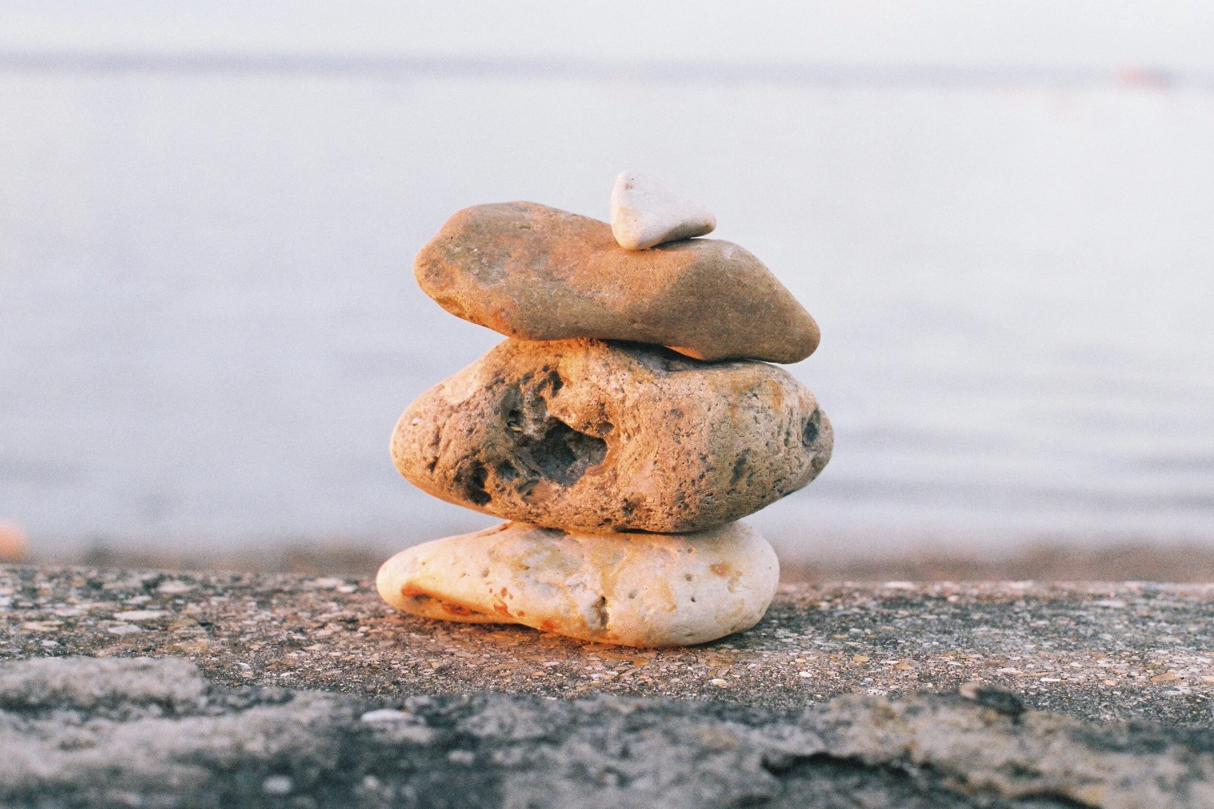 Stack of four smooth stones on a concrete surface by the water.