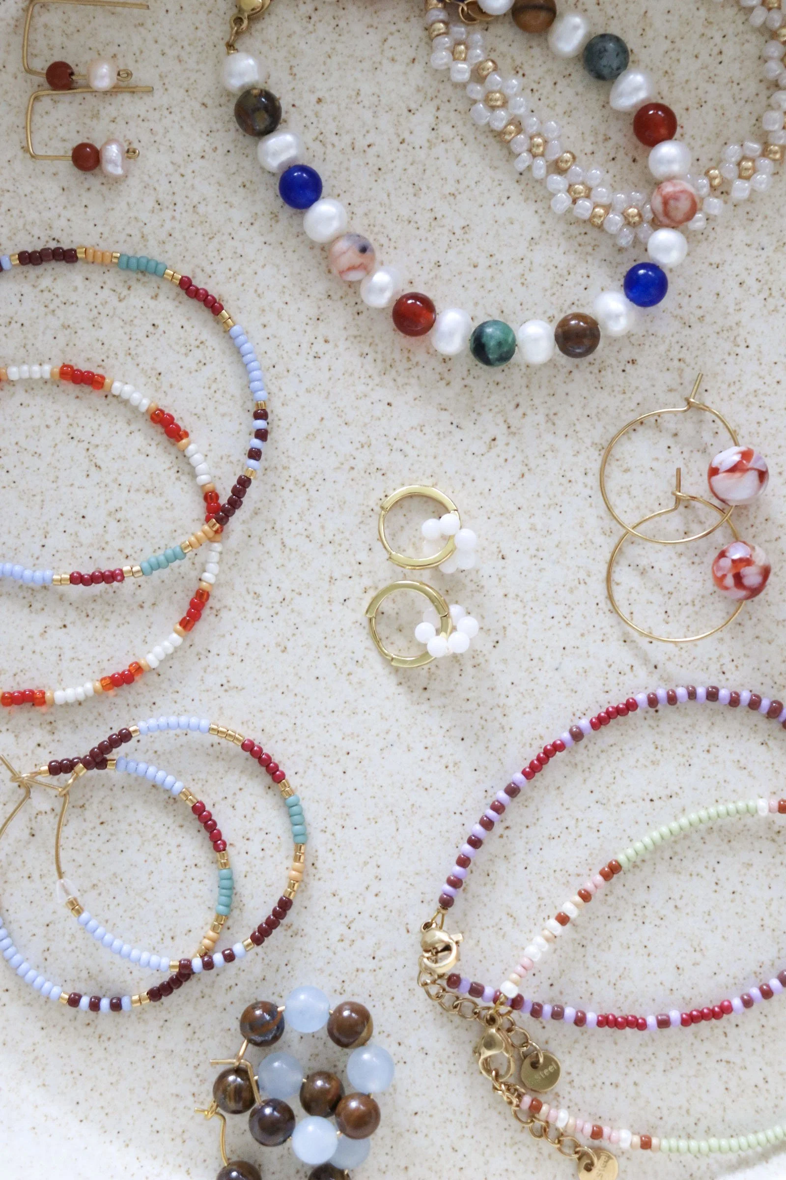 Various beaded jewelry including necklaces, bracelets, and earrings displayed on a light surface.