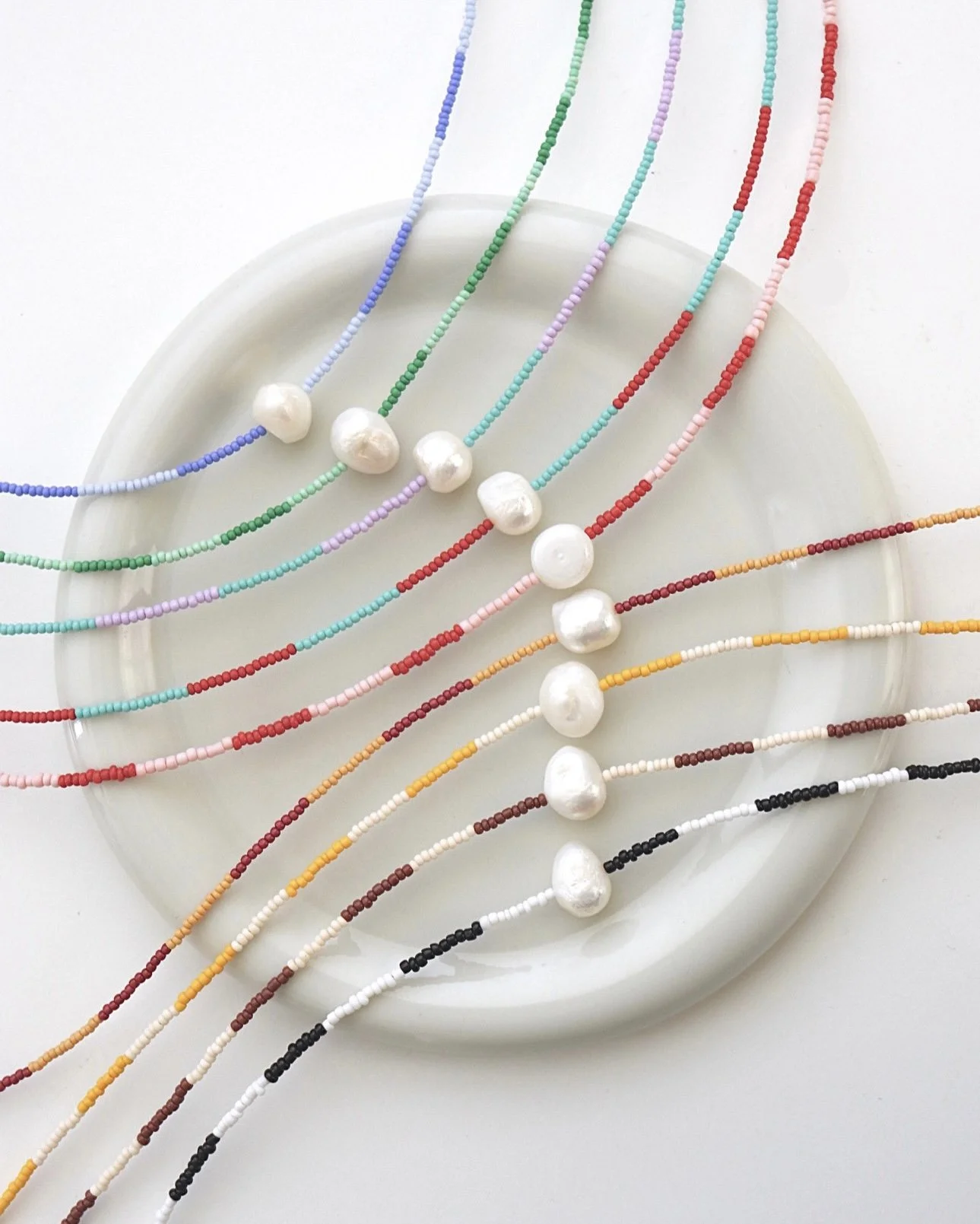 Colorful beaded necklaces with large white pearls arranged on a white plate.