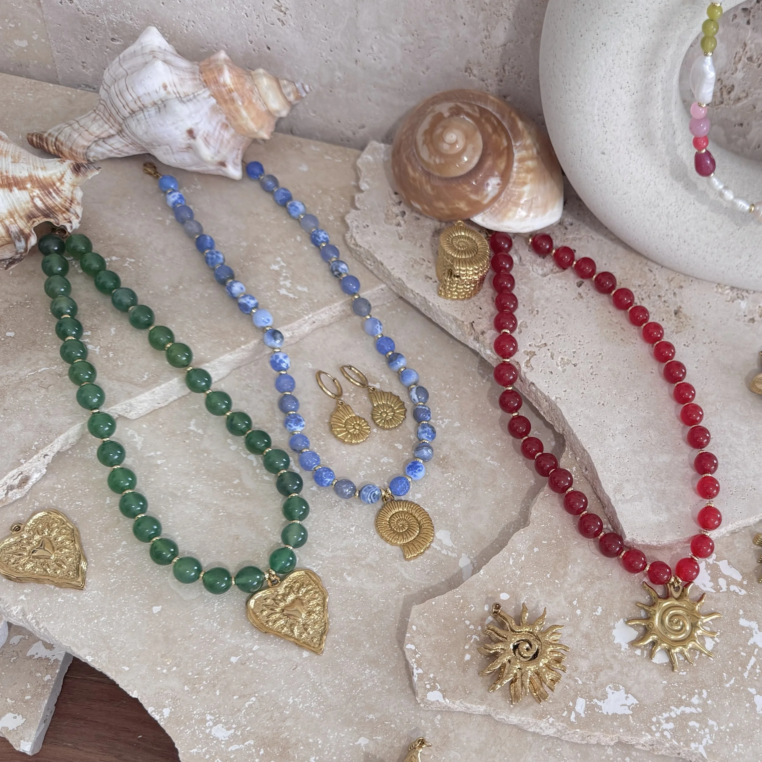 Arranged decorative jewelry including seashells and beads on a stone surface.