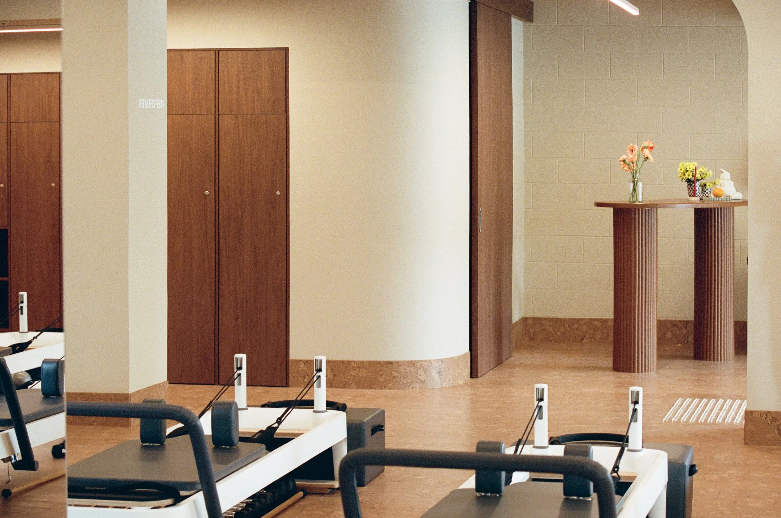 Fitness room with Pilates machines in the foreground, wooden cabinets on the left, and a small table with flowers and decorations in the background.