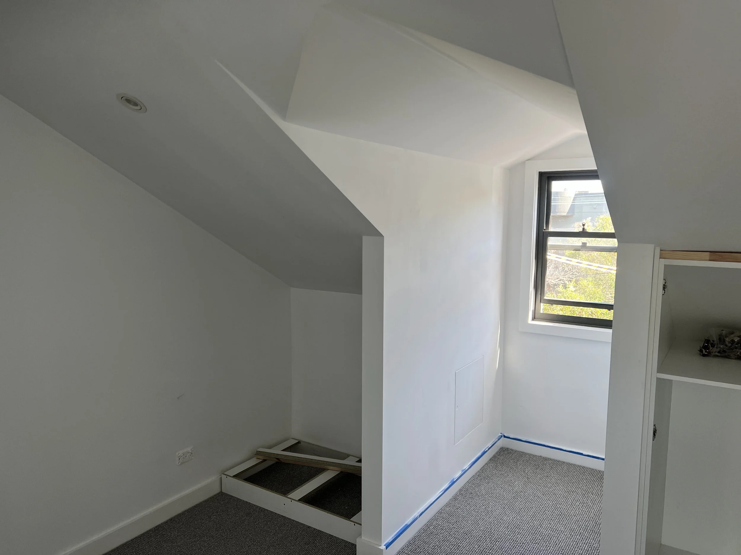 Empty room with a window letting in natural light and a partially assembled white desk or table.