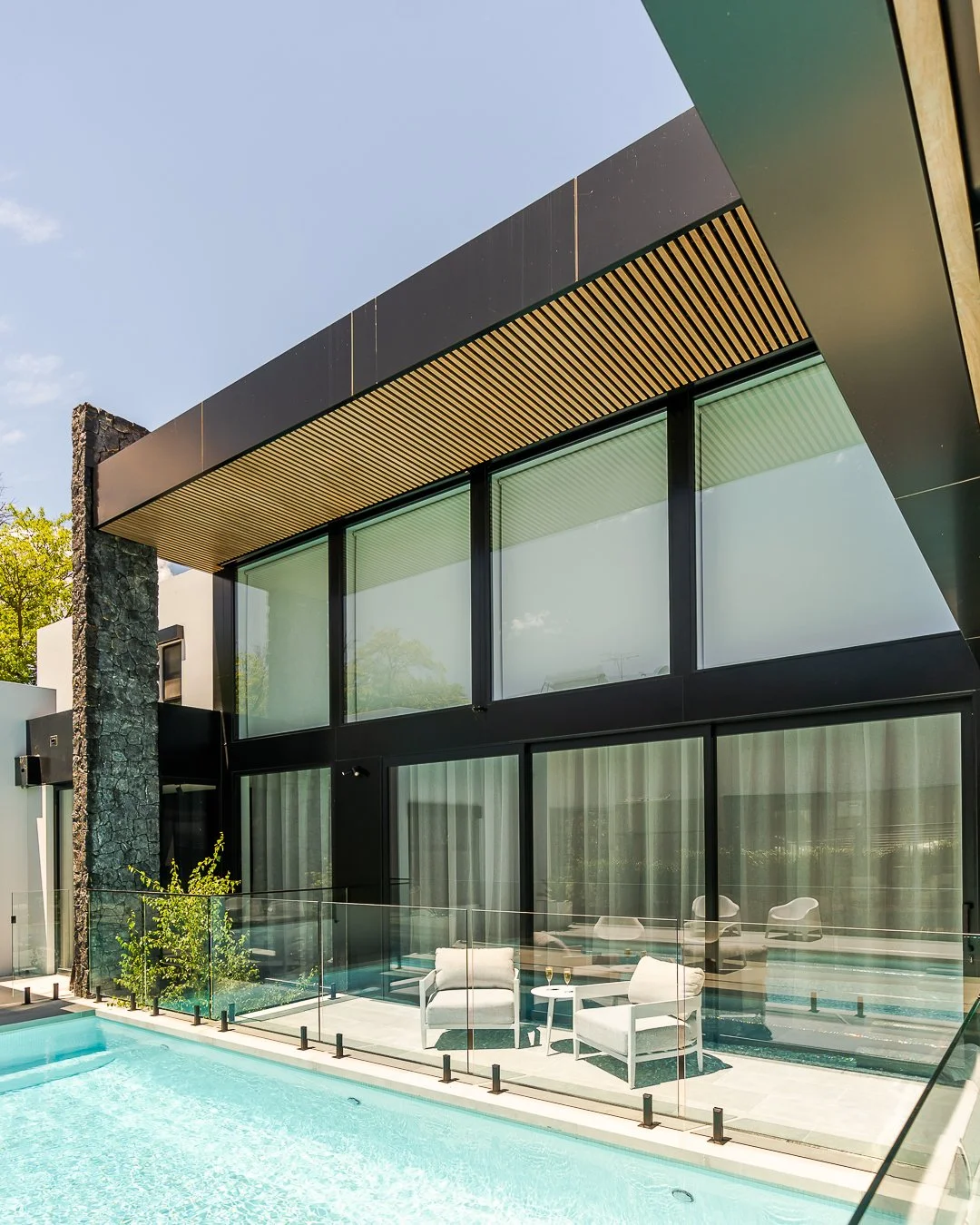 Modern house with large glass windows and a swimming pool in the foreground.