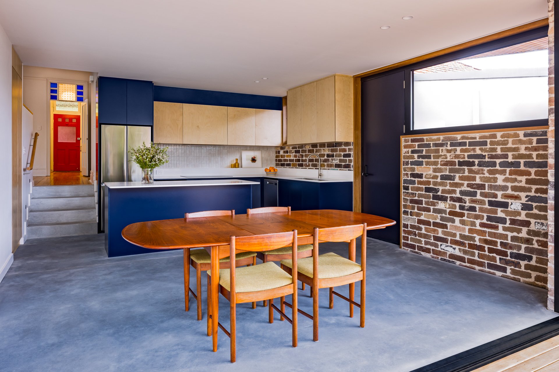 Interior view of a modern kitchen with a brick wall, wooden cabinetry, a blue and wood color scheme, and a wooden dining table with chairs.