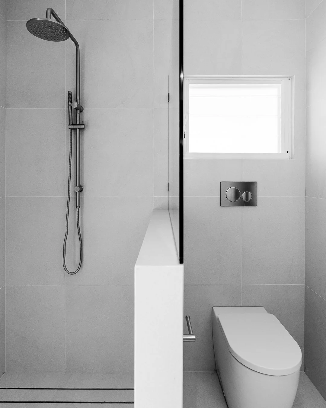 Modern bathroom with walk-in shower and toilet, white tiled walls, small window, and minimalistic fixtures.