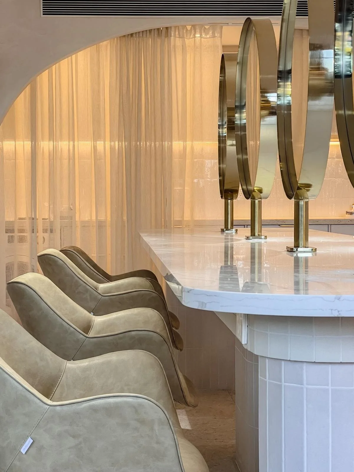 Modern cafe interior with a white marble counter, beige chairs, and decorative gold and mirror accents.
