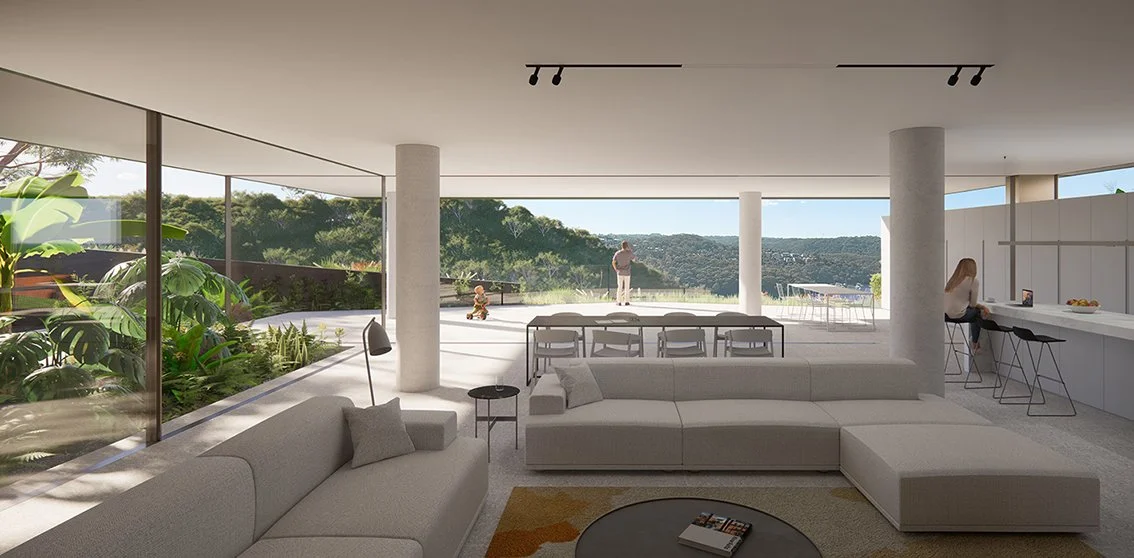 Modern living room with large glass windows overlooking a hillside, featuring a white sectional sofa, a small black side table, green plants outside, and a person sitting at a kitchen island.