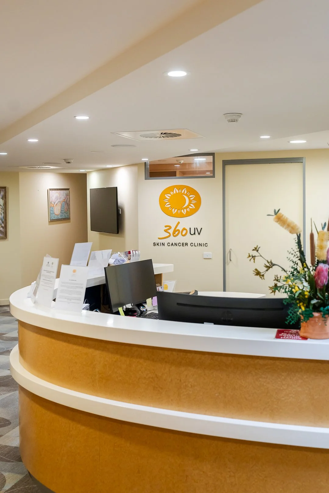 Reception desk at 360 UV Skin Cancer Clinic with a yellow logo, flower arrangement, and informational papers on the counter.