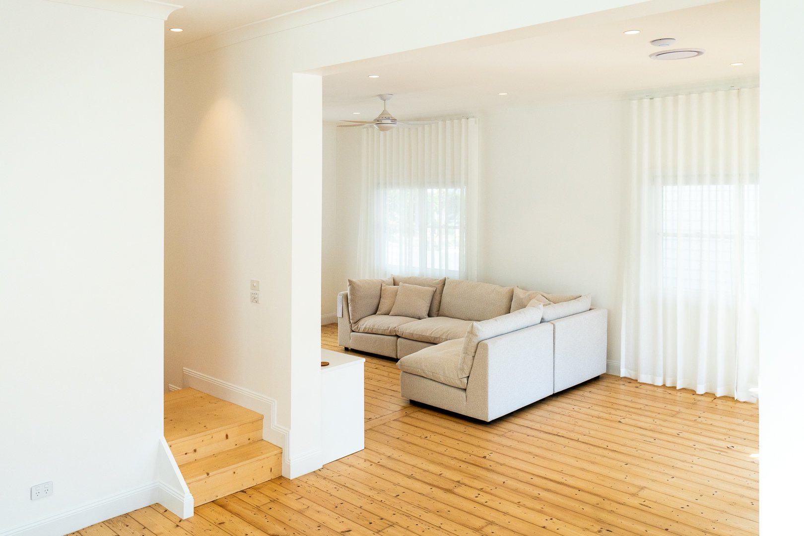 Bright living room with cream sofa, wooden floors, white curtains, and natural light.