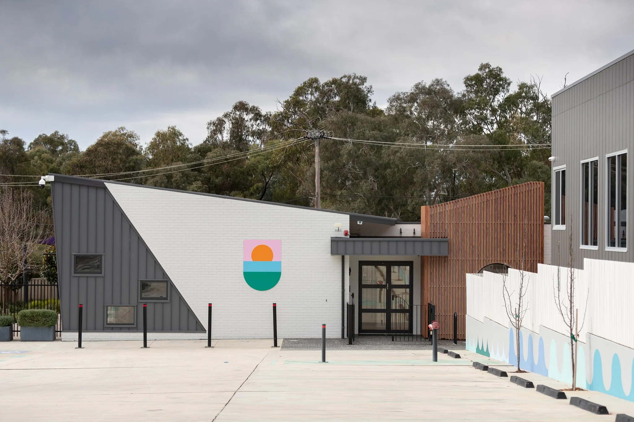 A modern building with a painted wall mural of a sunset over waves, with trees and a cloudy sky in the background.