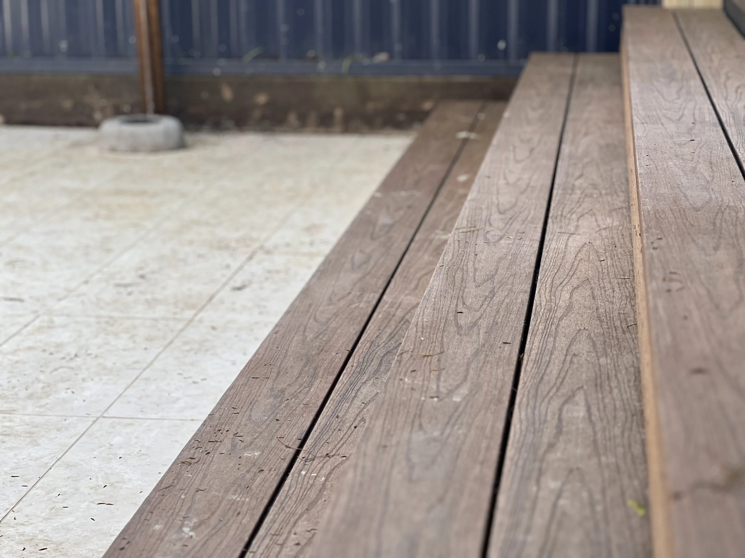 Close-up of a wooden bench with a metal fence and concrete base in the background.