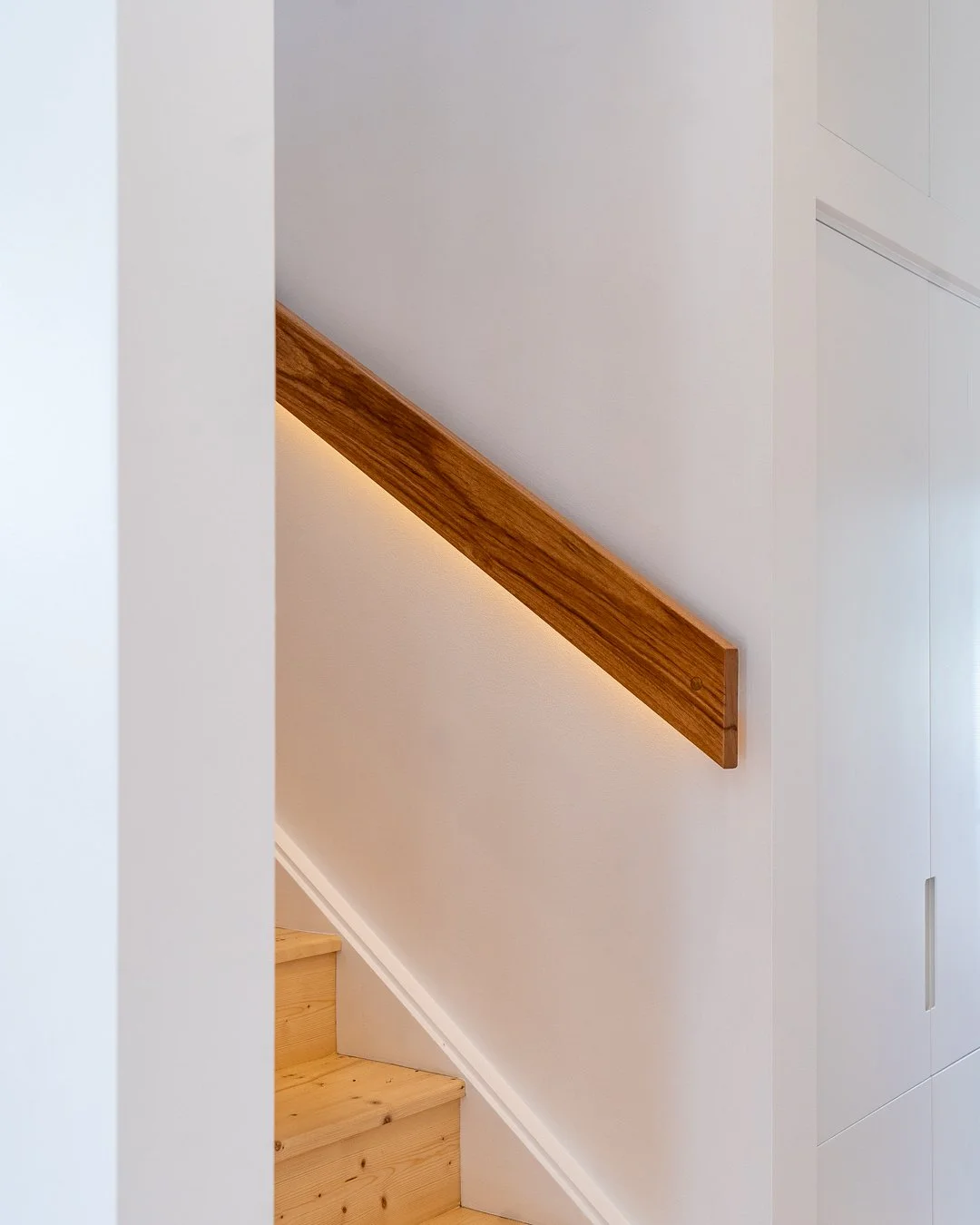 View of a staircase with wooden steps, a diagonal wooden handrail, and white walls.