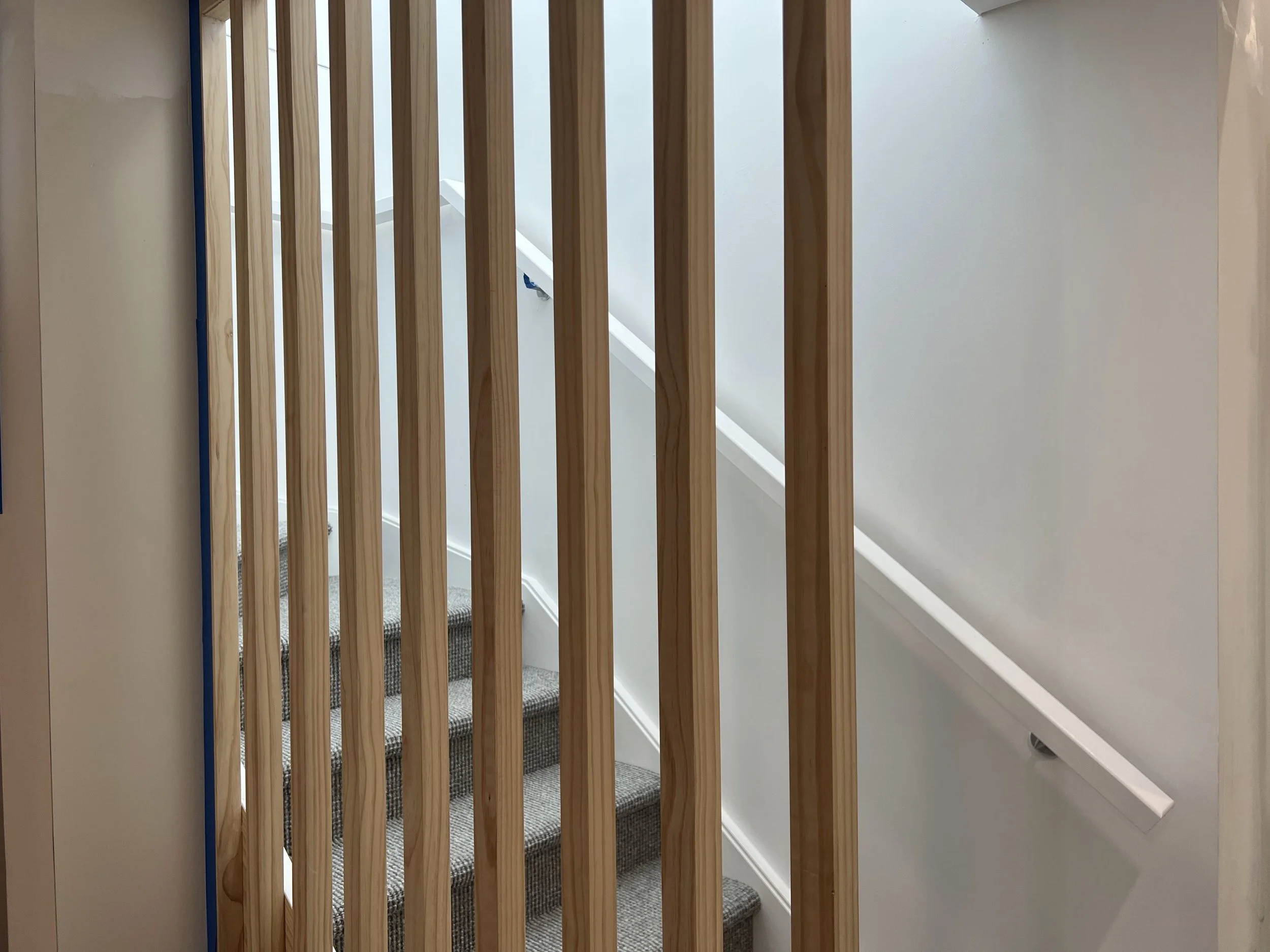 Wooden railing on a stairway with carpeted stairs and white walls.