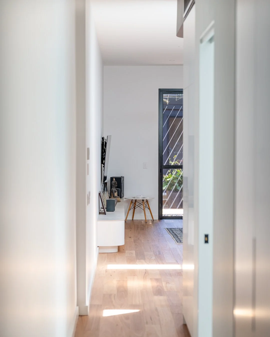 Empty hallway leading into a modern living space with a door to an outdoor balcony, wooden flooring, and minimalist decor.