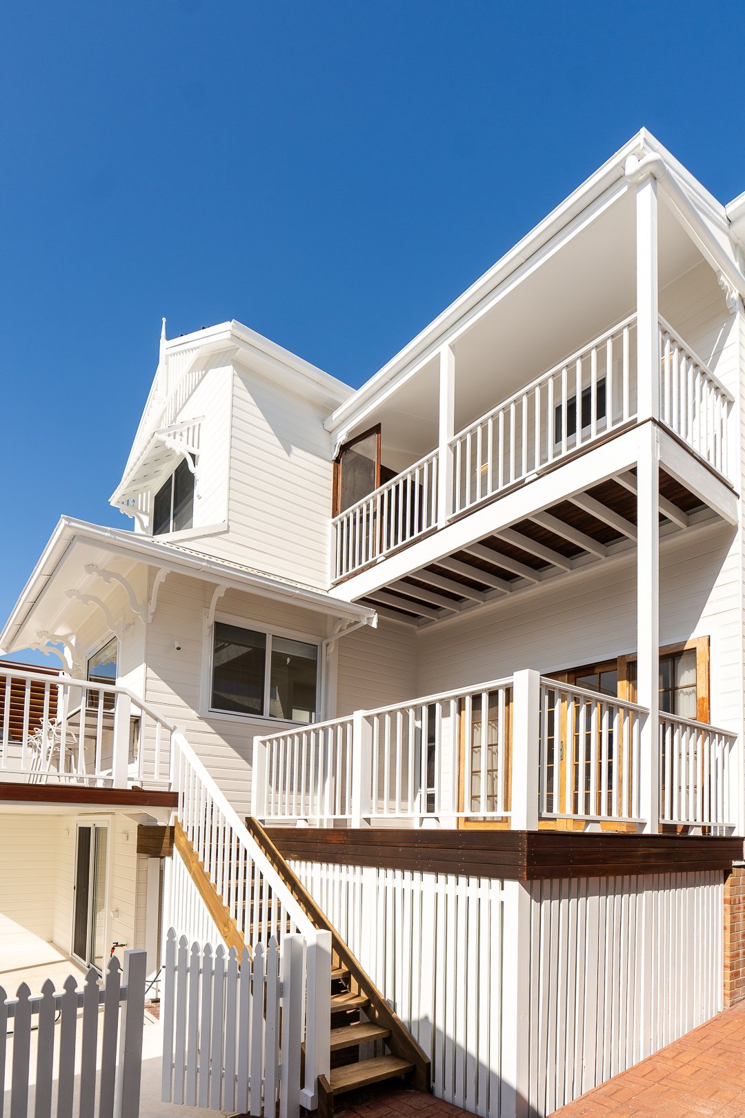 White multi-level house with decks, railings, and stairs, under a clear blue sky.