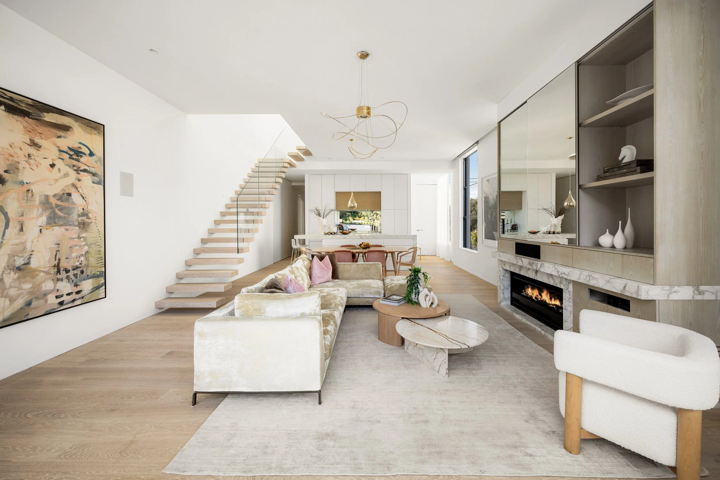 Modern living room with a fireplace, abstract art on the wall, a staircase, and seating area with cushions.