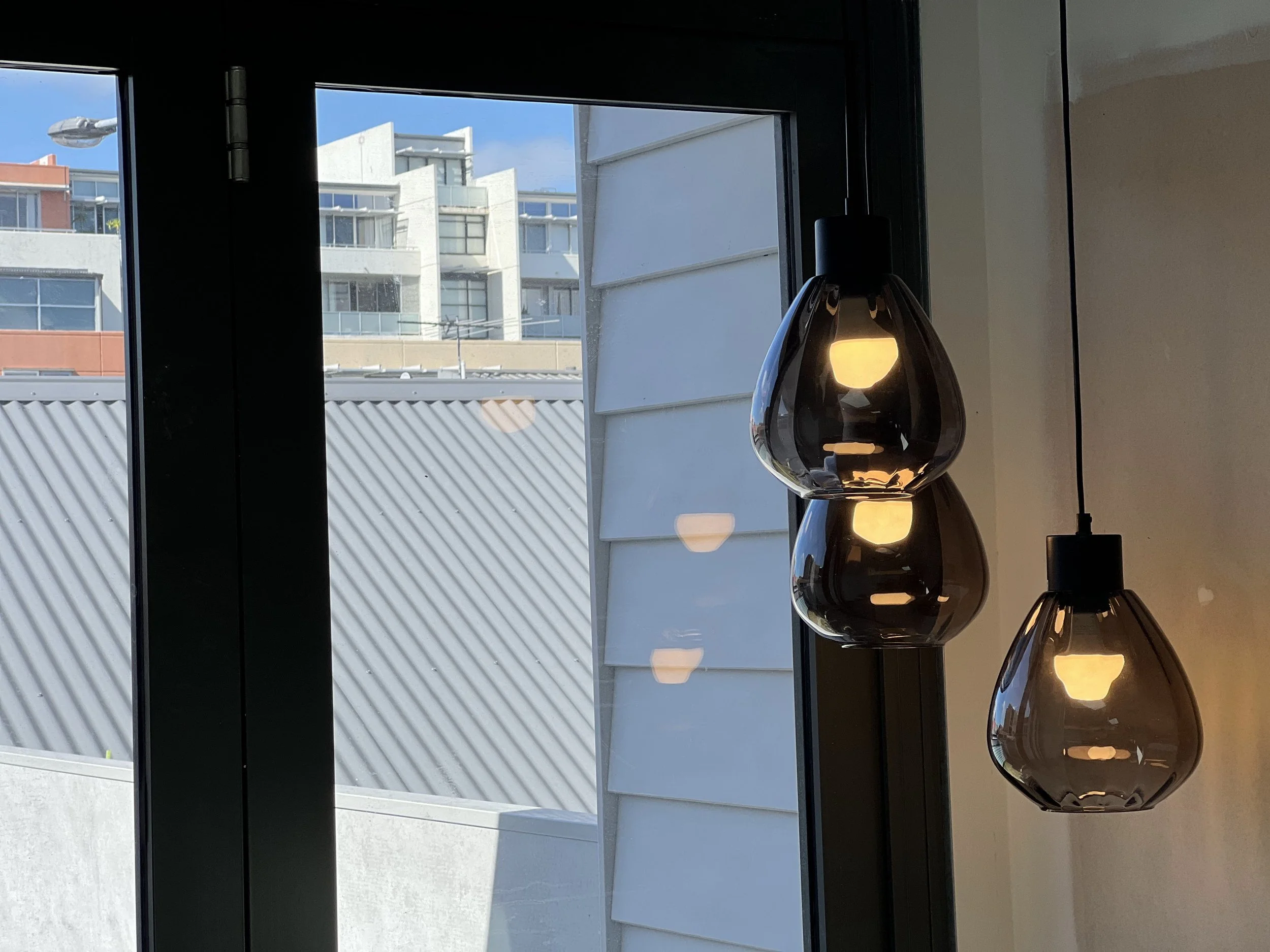 View of buildings through a glass window with a hanging black pendant lamp inside.