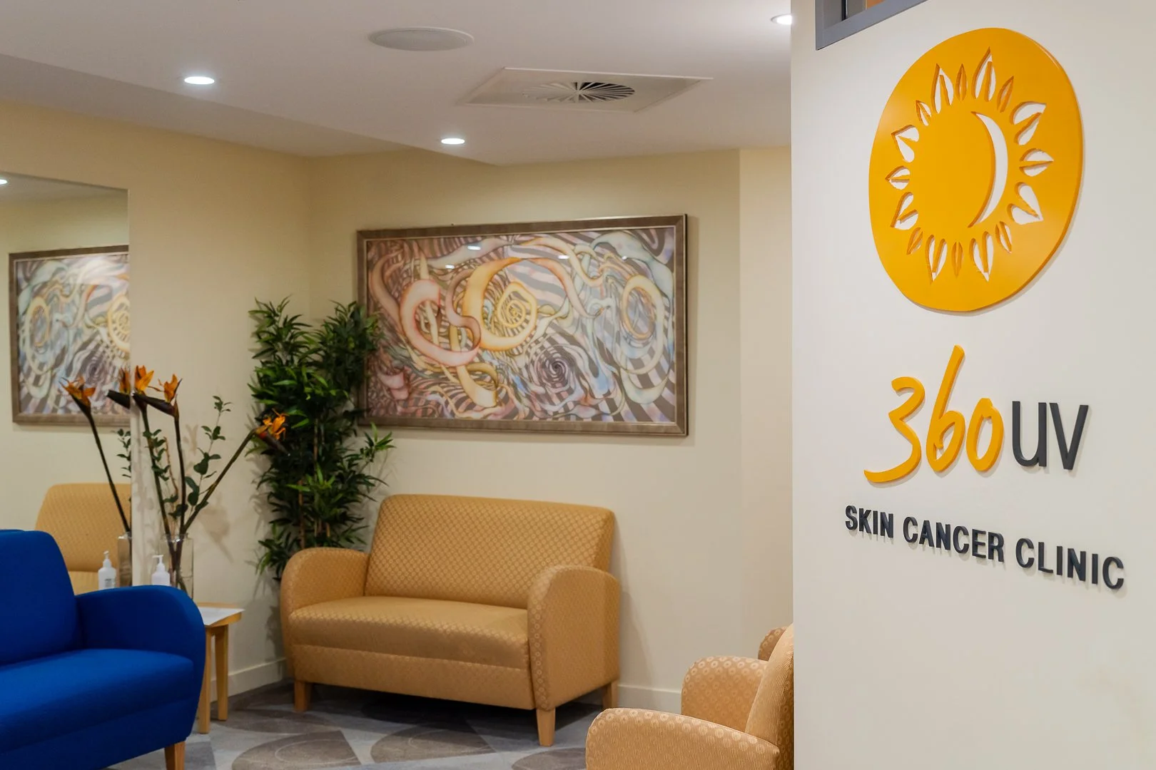 Waiting area at a skin cancer clinic with chairs, plants, and art on the walls, including a logo with a sun and moon on the signage.