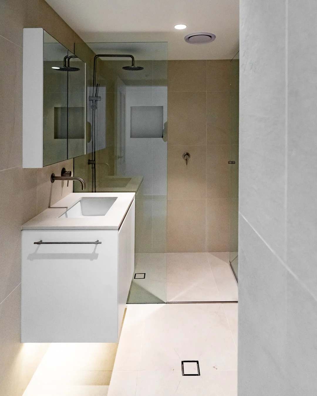 Modern bathroom with a white vanity, a single sink, beige tiled walls, and a glass-enclosed shower area with a rain shower head.