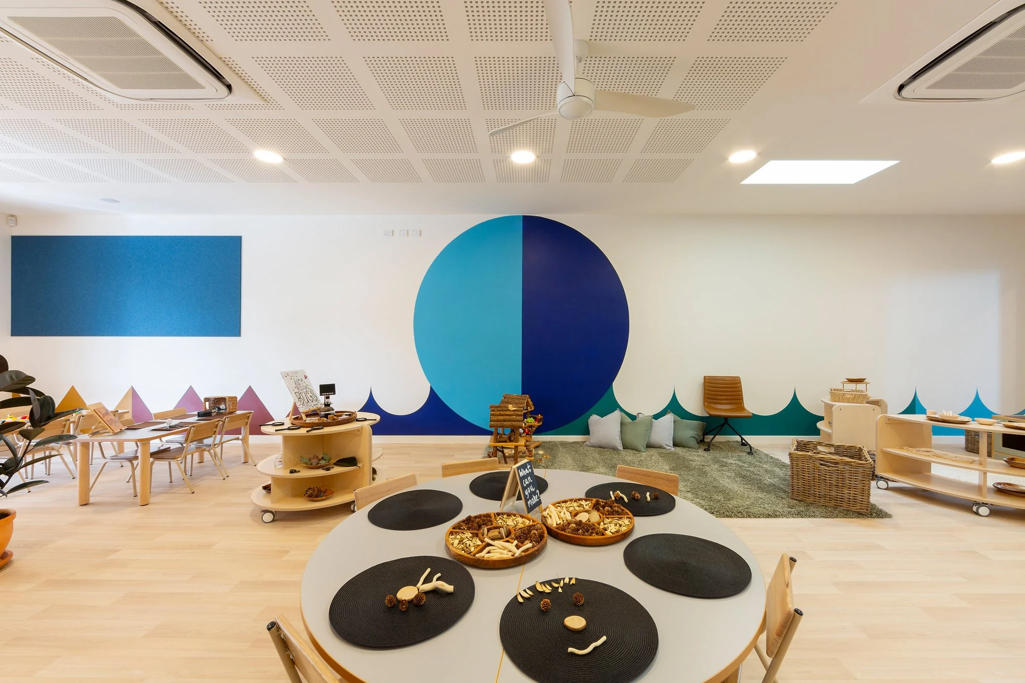Children's play area with tables, chairs, and educational toys, including a circular table with black mats and animal bones.