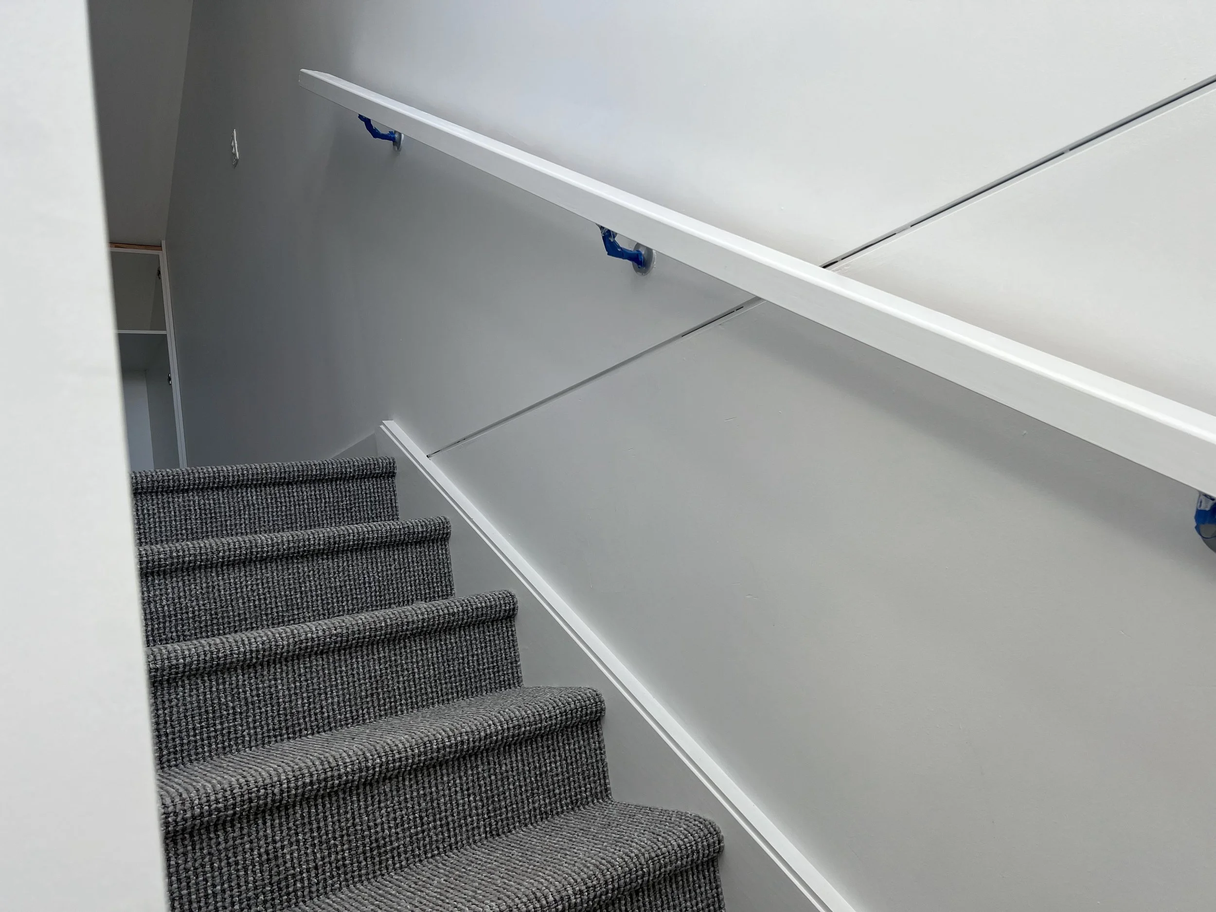 A staircase with dark gray and black patterned carpeted steps leading upward, visible from below, with a white wall and a doorframe on the side, and a white railing along the staircase.