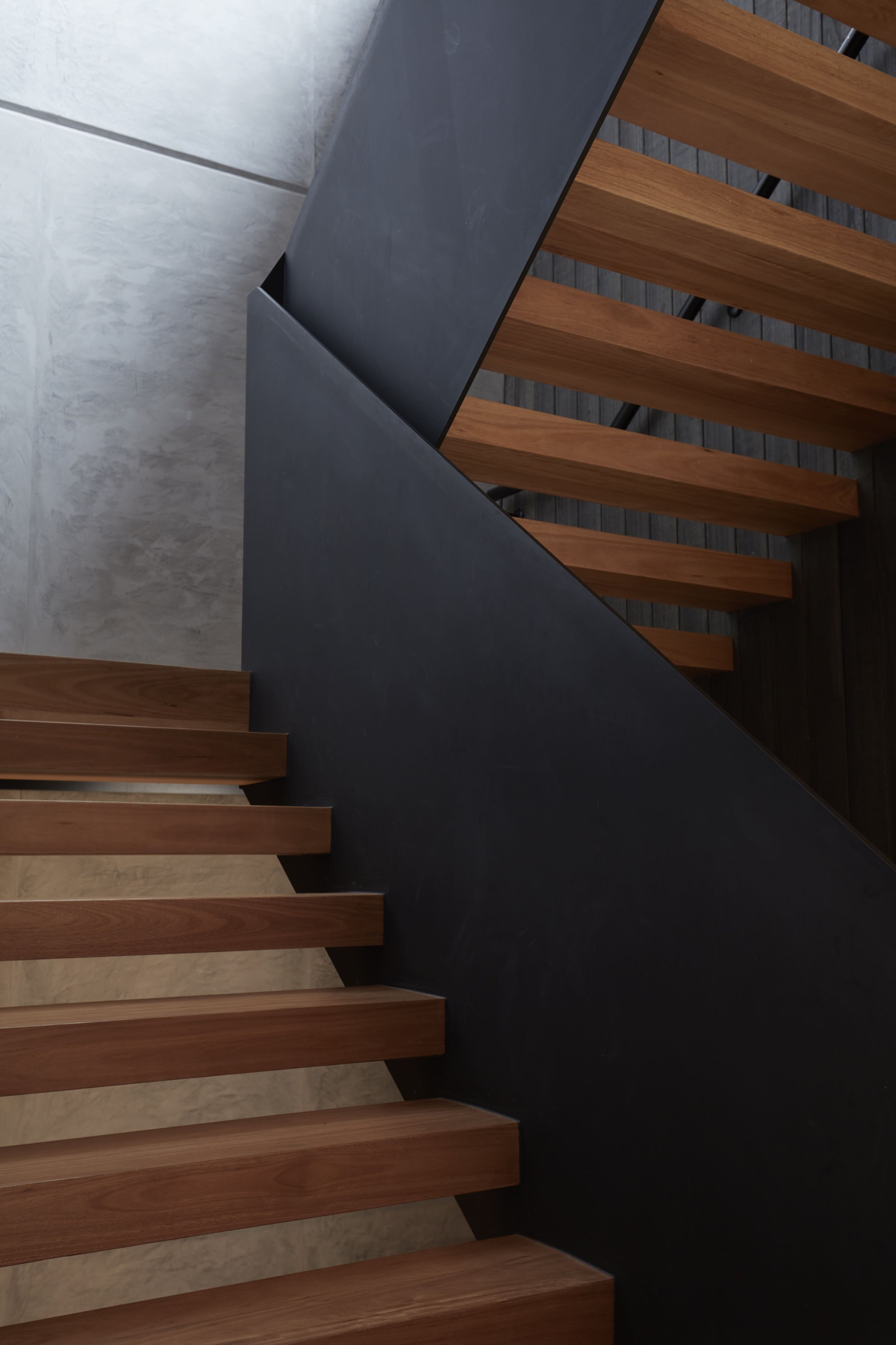 Top view of a staircase with wooden treads and a metal railing, set against a white wall.