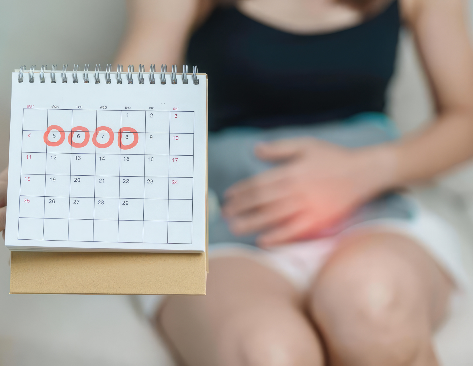 Woman tracking her menstrual cycle on a calendar while holding her abdomen — acupuncture for women's health in NW Calgary