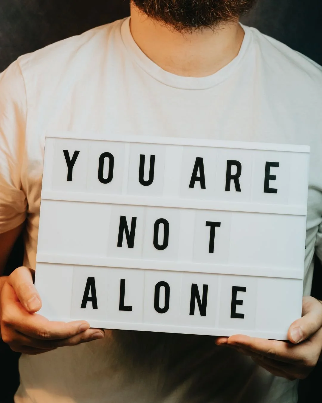 man holding sign that says you are not alone