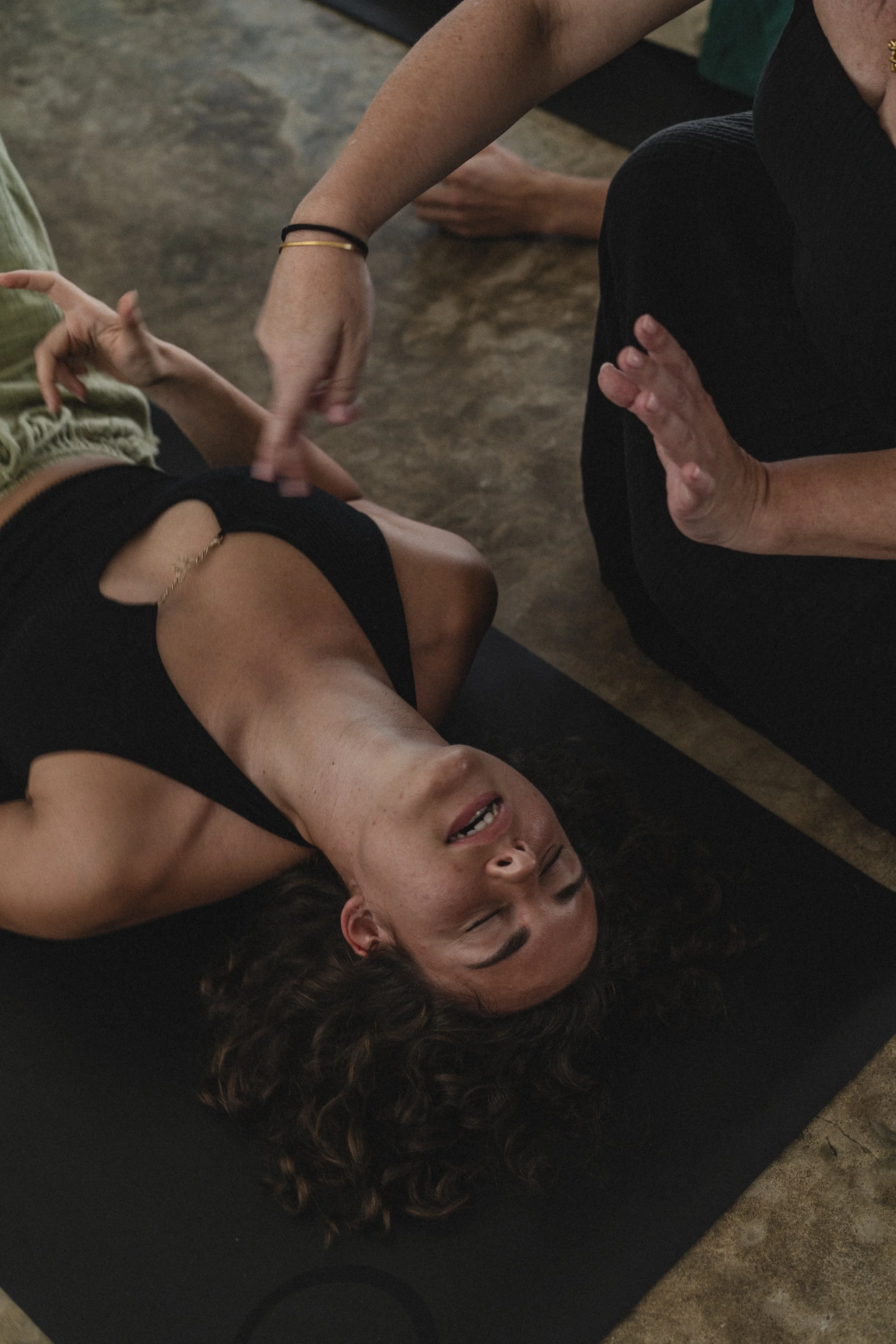 A woman in a patterned dress standing outdoors in front of a large wooden tribal sculpture large face figure with carved features, in a lush garden with tropical plants and trees.