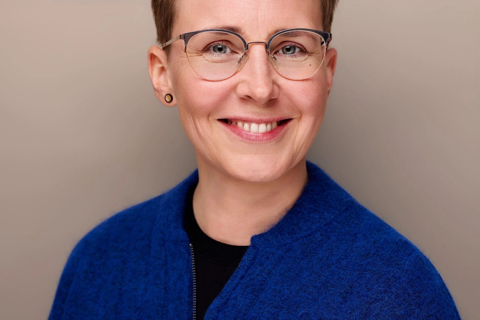 Eine Frau mit Brille und blauem Pullover lächelt auf ihrem Bewerbungsbild