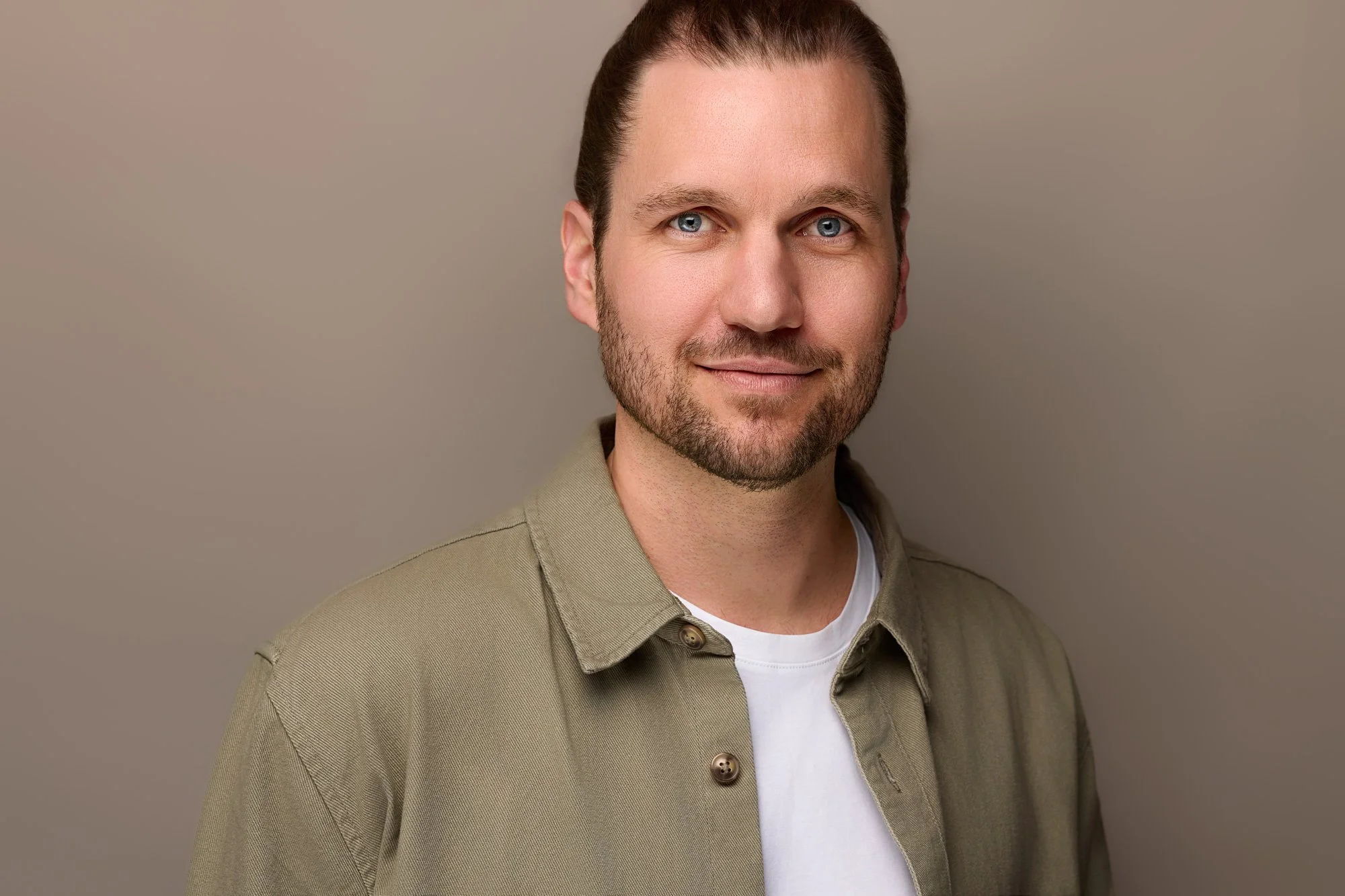 Ein Mann posiert vor einen erdfarbenen Hintergrund für den Fotografen