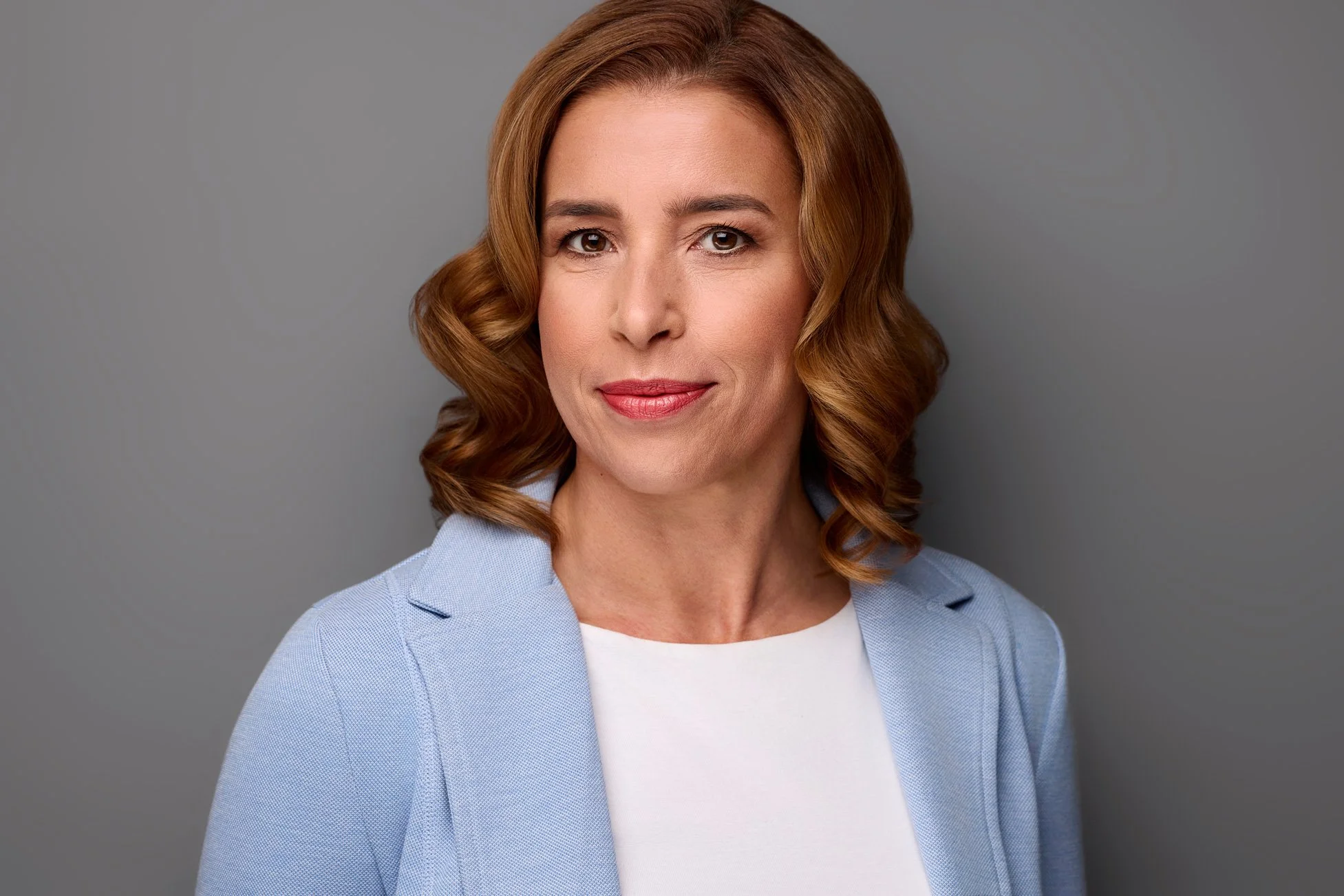 Eine Frau posiert für ihre Bewerbungsfotos in Leipzig vor einem grauen Hintergrund