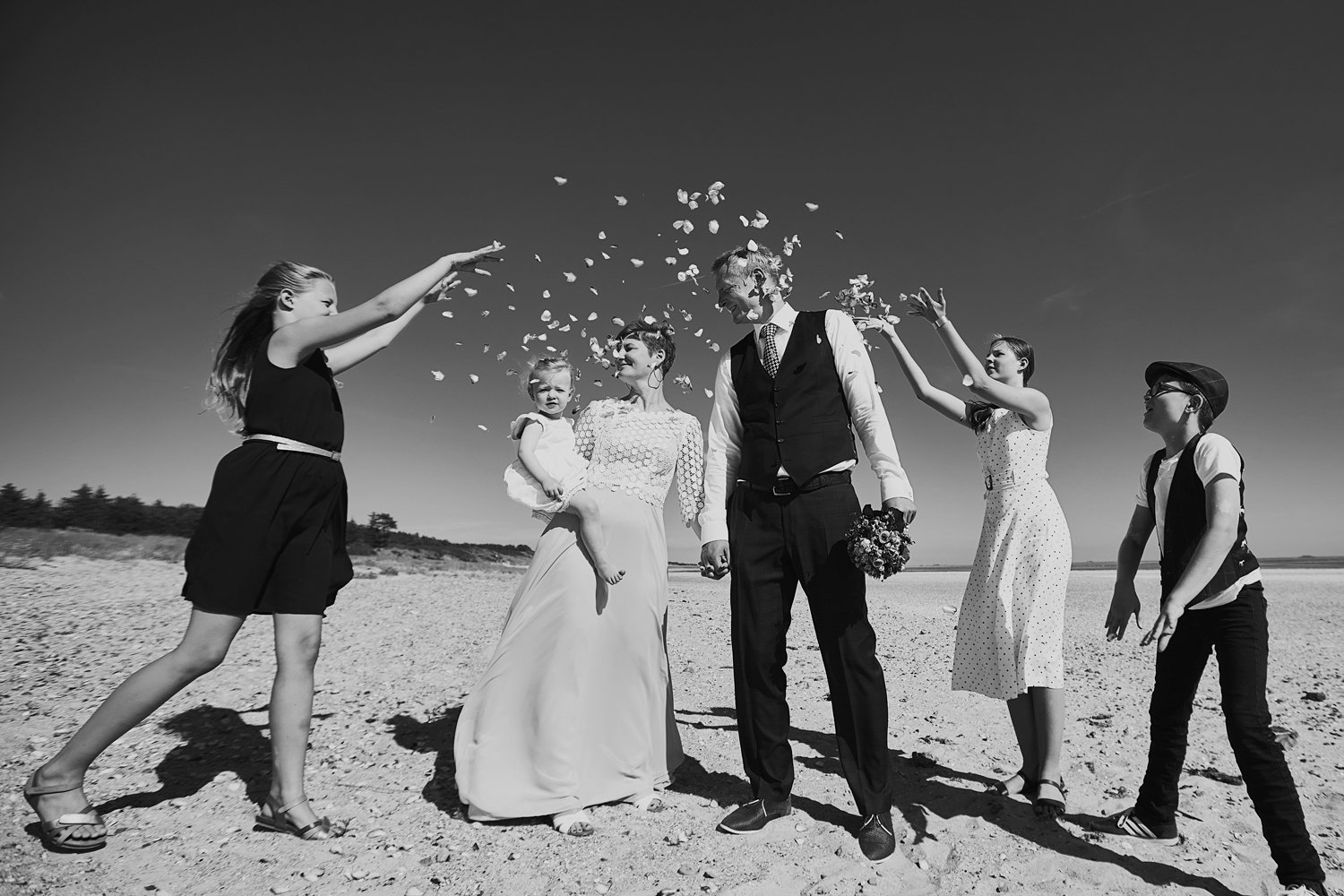 Die Kinder bewerfen ihre Eltern, die grad geheiratet haben, mit Blüten am Strand