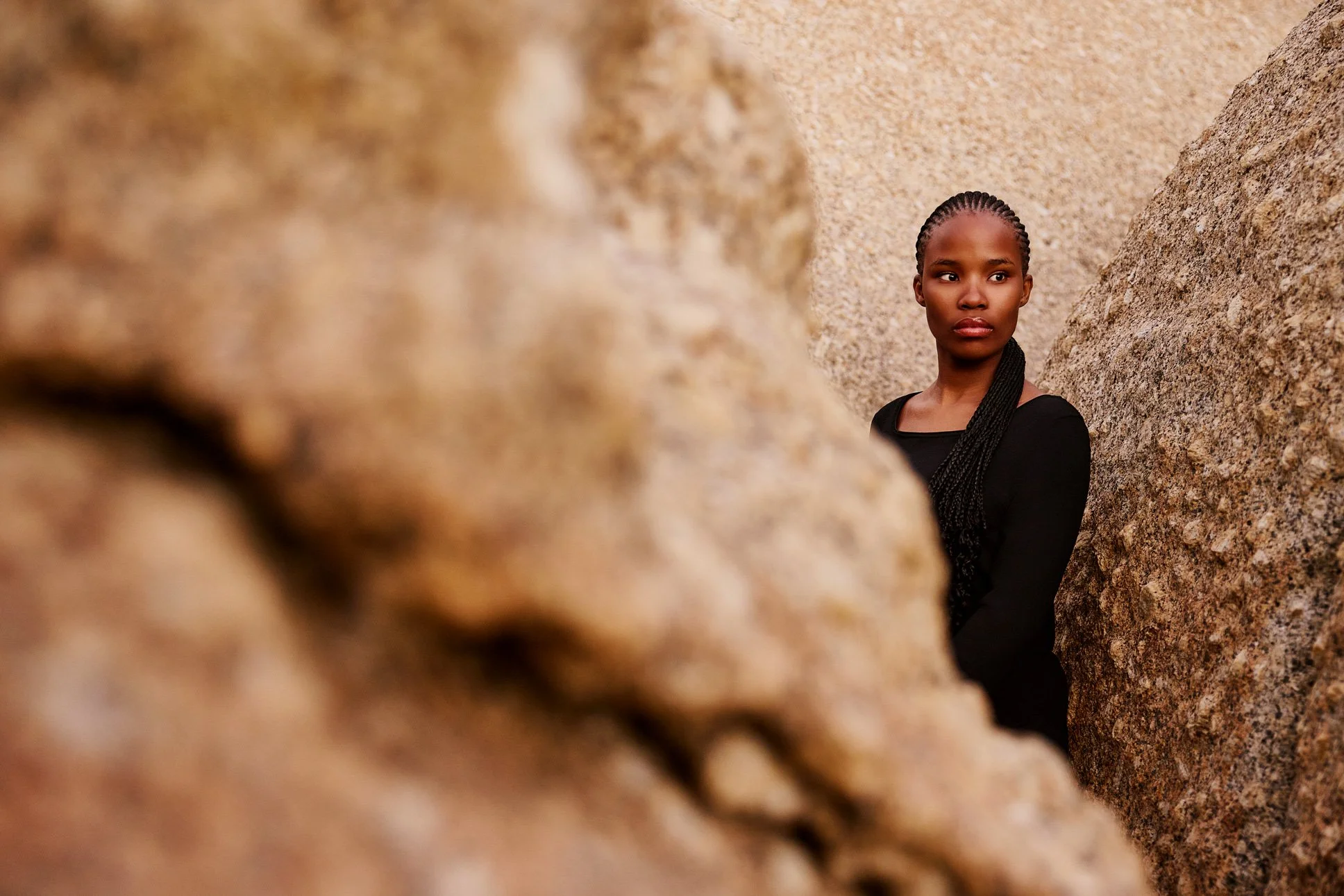 Ein Portraitfoto von einer jungen Frau schwarz gekleidet, die in einer Felsennische steht